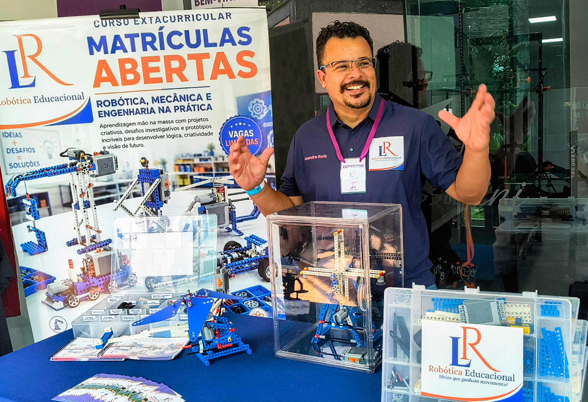 Exposição da LR Robótica Educacional com o professor Leandro Roriz, Kits LR e protótipos de Engenharia e Mecânica expostos sobre a mesa